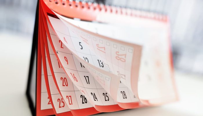 A imagem mostra um calendário de mesa de bordas vermelhas sendo folheado.
